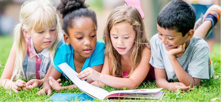 Four kids reading a book on the grass